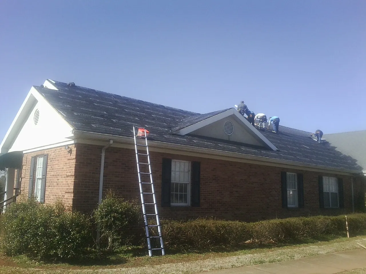 Crew tearing shingles off a brick ranch roof with a ladder set — Metal Roof Repair work by our crew in Sumerduck
